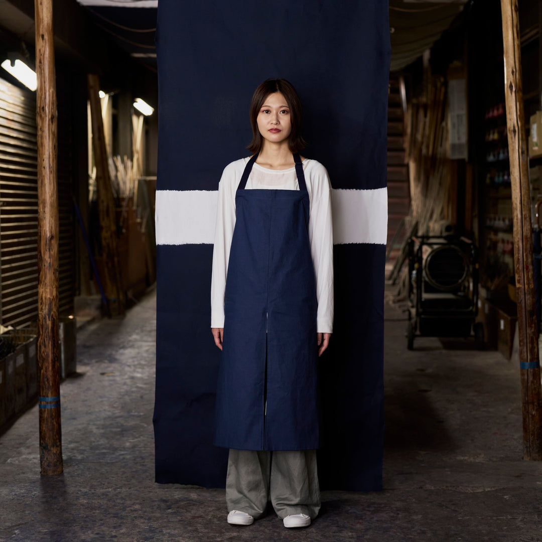 Model wearing navy Japanese front split apron standing in workshop with indigo fabric backdrop