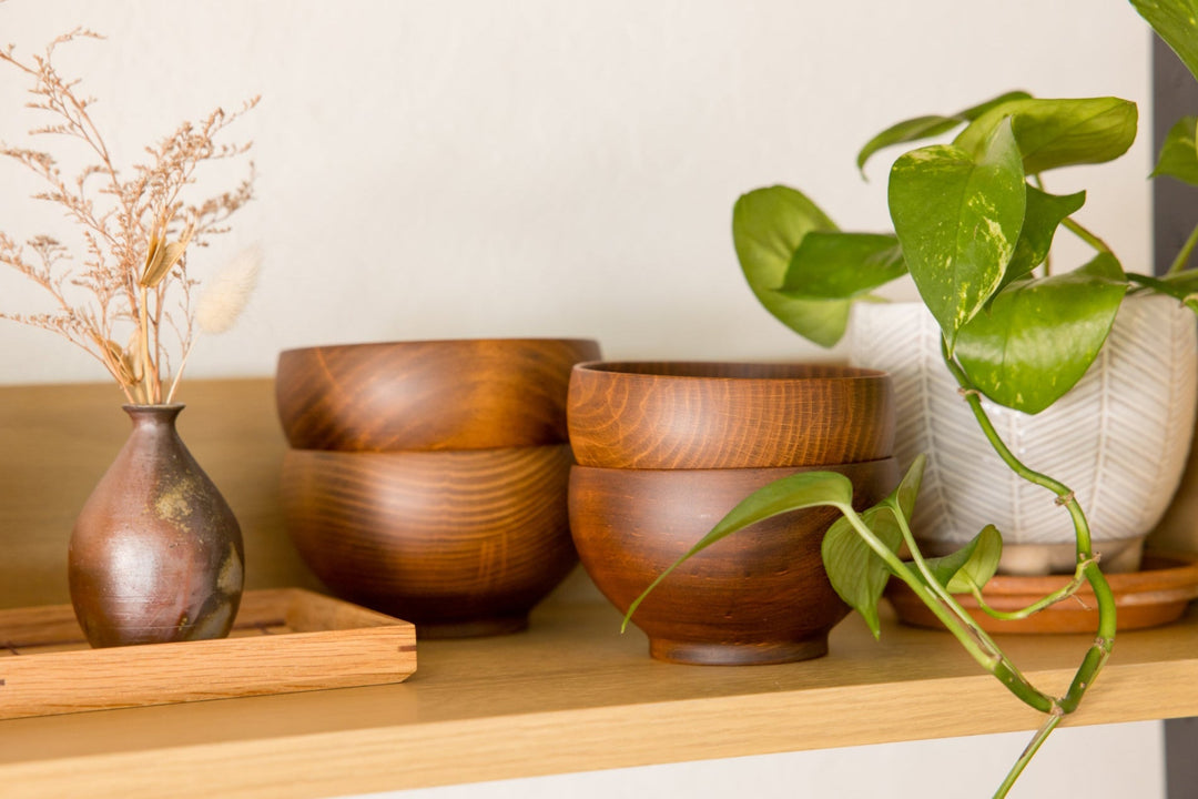 Warm wooden bowls displayed on a shelf with a small ceramic vase and a green potted plant creating a natural cozy scene
