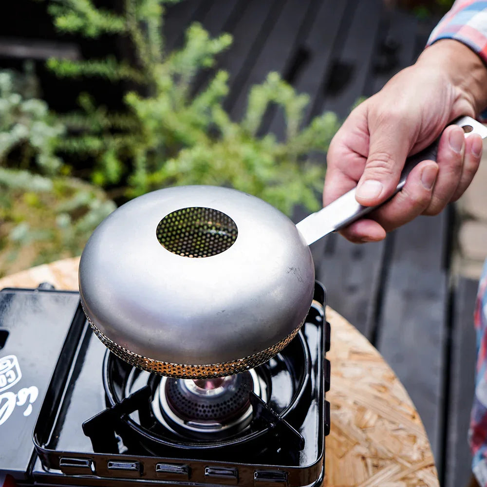 Stainless steel hand coffee roaster placed over a portable gas stove for outdoor coffee roasting.
