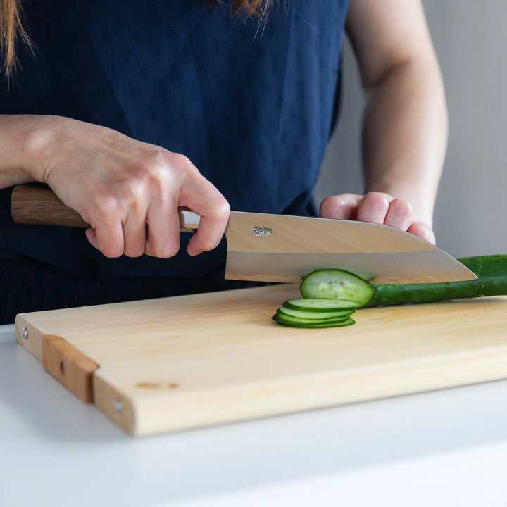 Tosa Ginsan Stainless Funayuki Knife slicing cucumber on a hinoki cutting board, showing its sharpness and balance.