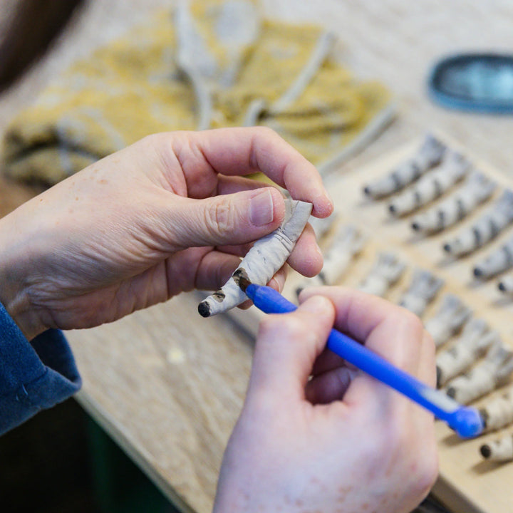 Artisan painting details onto a small ceramic piece shaped like bamboo during the hand finishing process