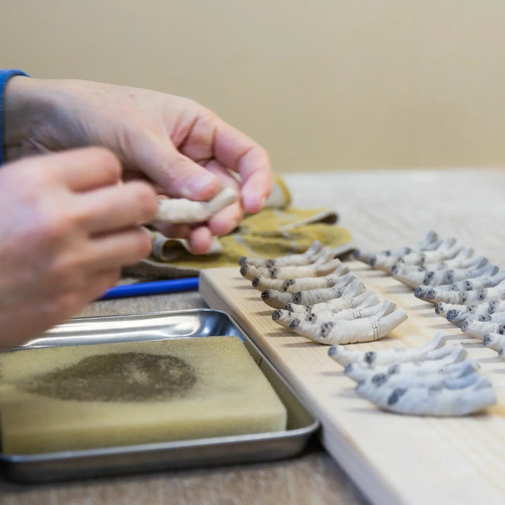 Artisan refining small ceramic pieces shaped like bamboo during detailed handwork in the workshop