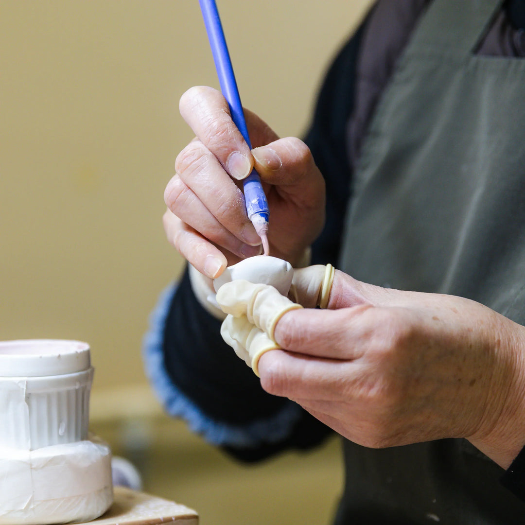 Artisan applying colored slip to a small ceramic piece with a brush during detailed hand painting work