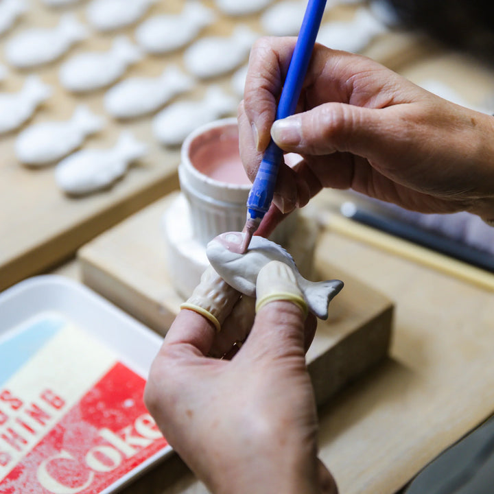 Artisan painting a fish shaped ceramic piece with colored slip during the delicate hand finishing process