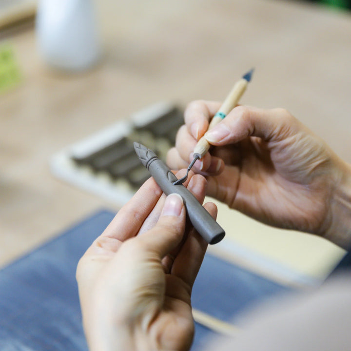 Artisan carving details into a small ceramic piece with precision tools during the hand shaping process