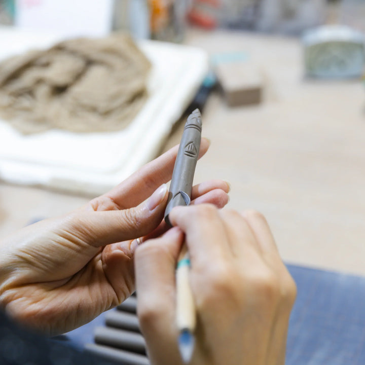 Artisan engraving patterns onto a slender ceramic piece with careful handwork in the workshop