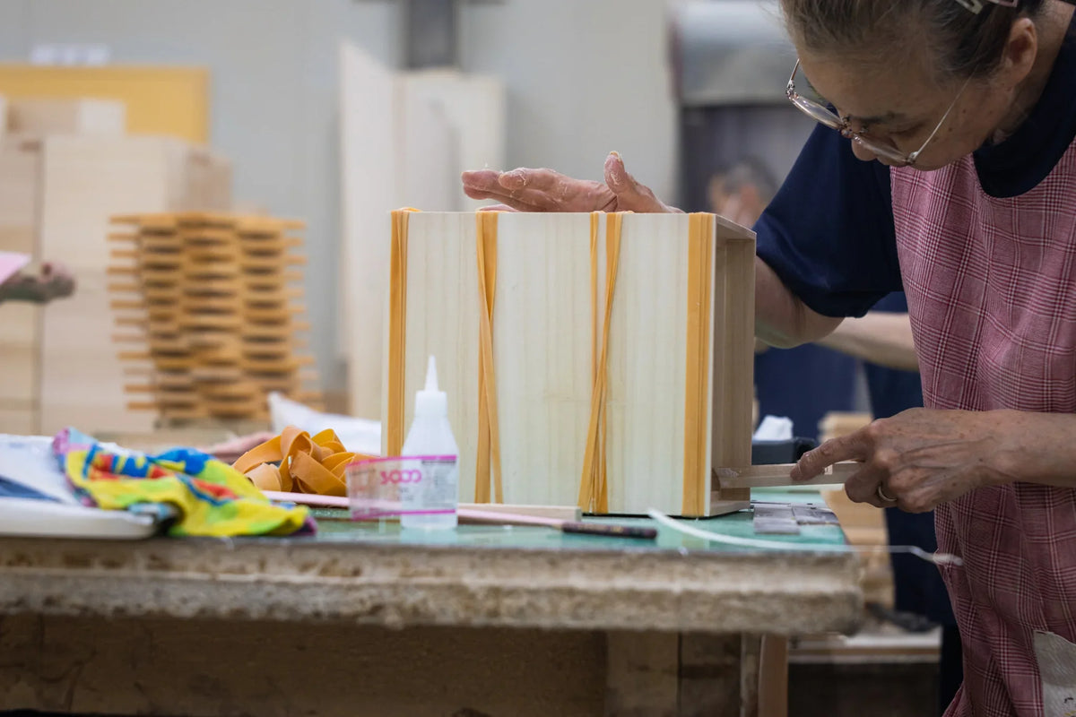 Japanese craftsperson assembling a paulownia wooden box held together with rubber bands at Masuda Kiribako workshop in Fukuoka Japan