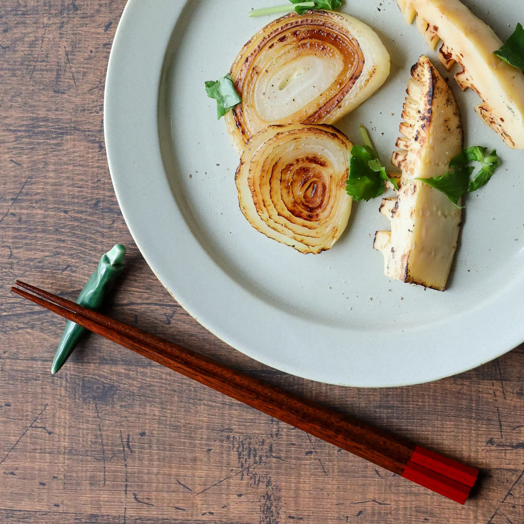 A pair of wooden octagonal Japanese chopsticks with red lacquered ends, resting beside a Japanese meal.