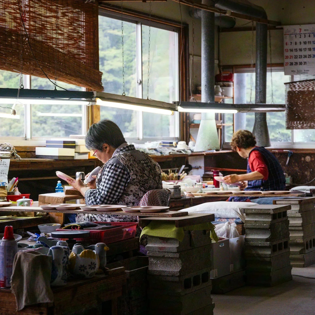 Artisans hand painting kids tableware in a quiet workshop setting with tools and plates arranged across the workspace