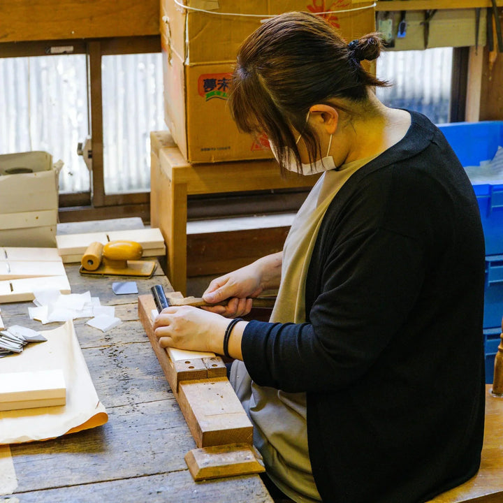 Craftsperson hand shaping hinoki wood pieces at a traditional Japanese woodworking bench