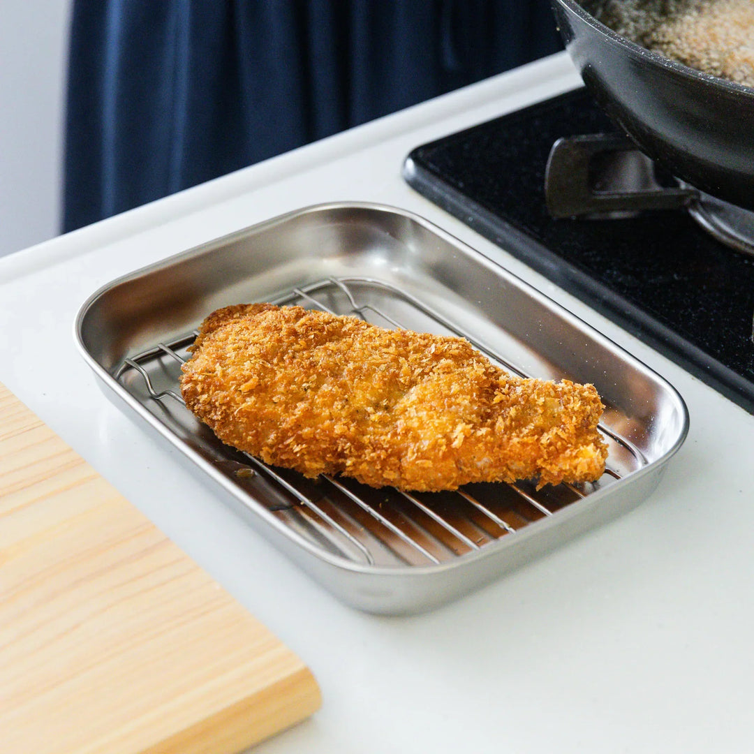 Freshly fried tonkatsu resting on a stainless prep tray with a wire rack, allowing excess oil to drain and stay crisp.