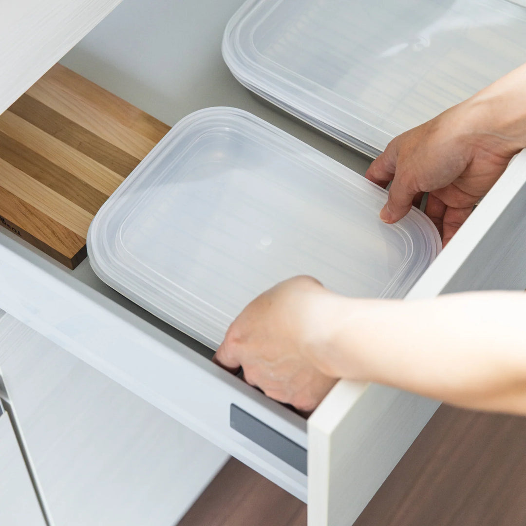 Nami placing stainless prep trays with lids into a kitchen drawer, showing compact and organized storage.