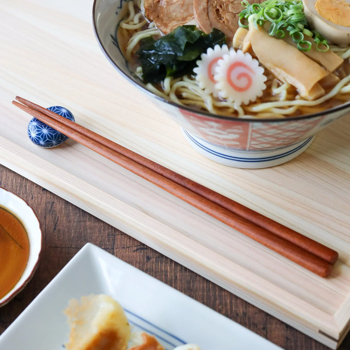 Premium zelkova wooden Japanese chopsticks resting on a blue porcelain chopstick rest.