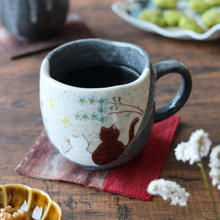 Ceramic mug with two cats under blooming tree soft cream and charcoal tones for cozy whimsical charm.