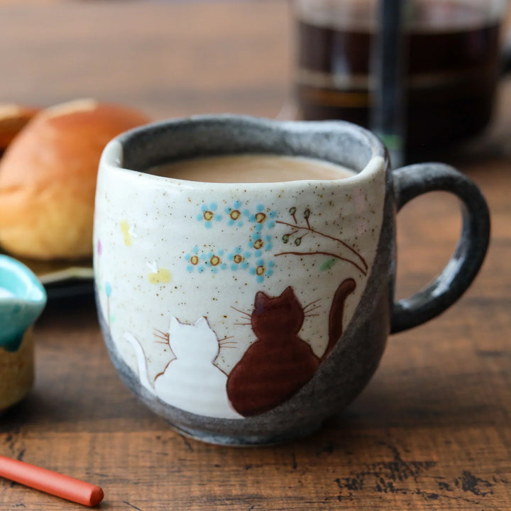 Ceramic mug with two cats under blooming tree soft cream and charcoal tones for cozy whimsical charm.