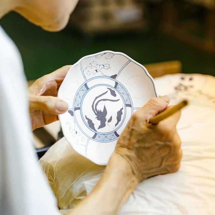 Hand painting traditional patterns on an unglazed Japanese porcelain plate at a kiln workshop.