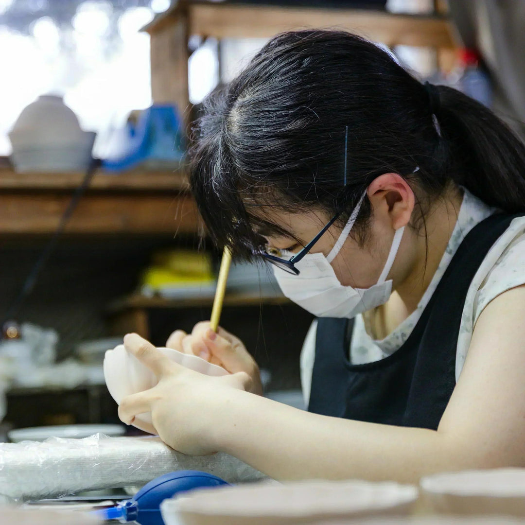 Artisan painting fine details on a scalloped ceramic bowl at a Japanese kiln workspace