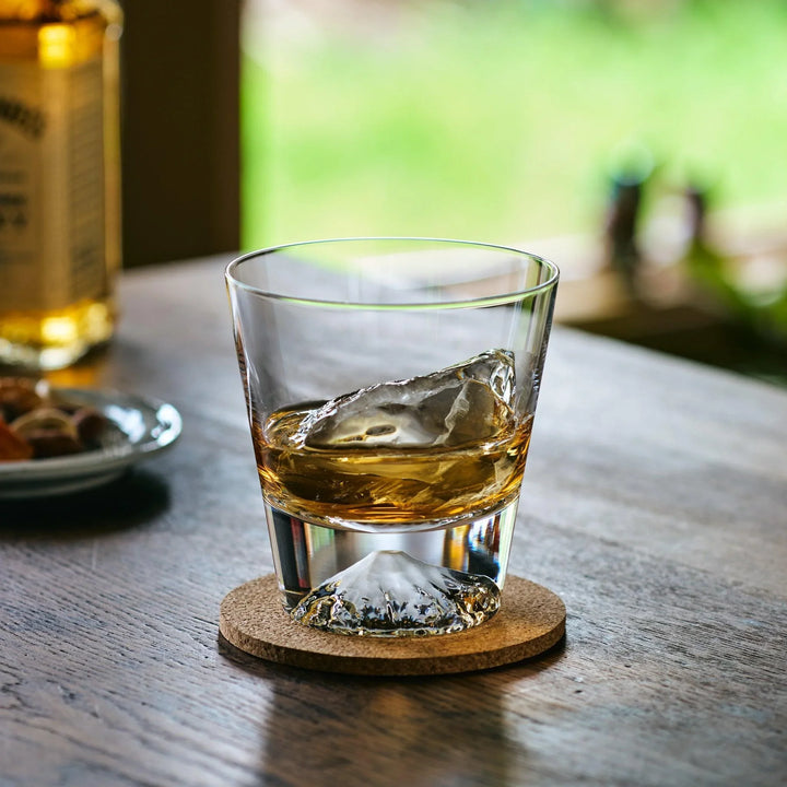 A Japanese whiskey glass with a Mt. Fuji base, filled with whiskey and ice, glowing in natural light.