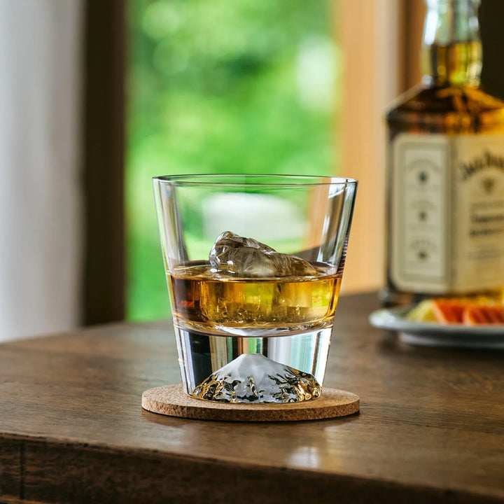 A Japanese whiskey glass with a Mt. Fuji-shaped base, filled with whiskey and ice, set on a wooden table.