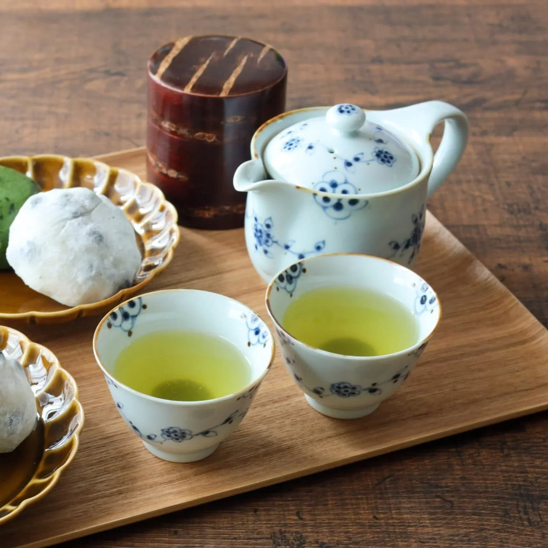 Wooden tray with floral teapot cups of green tea mochi desserts and bud vase creating serene tea setting.