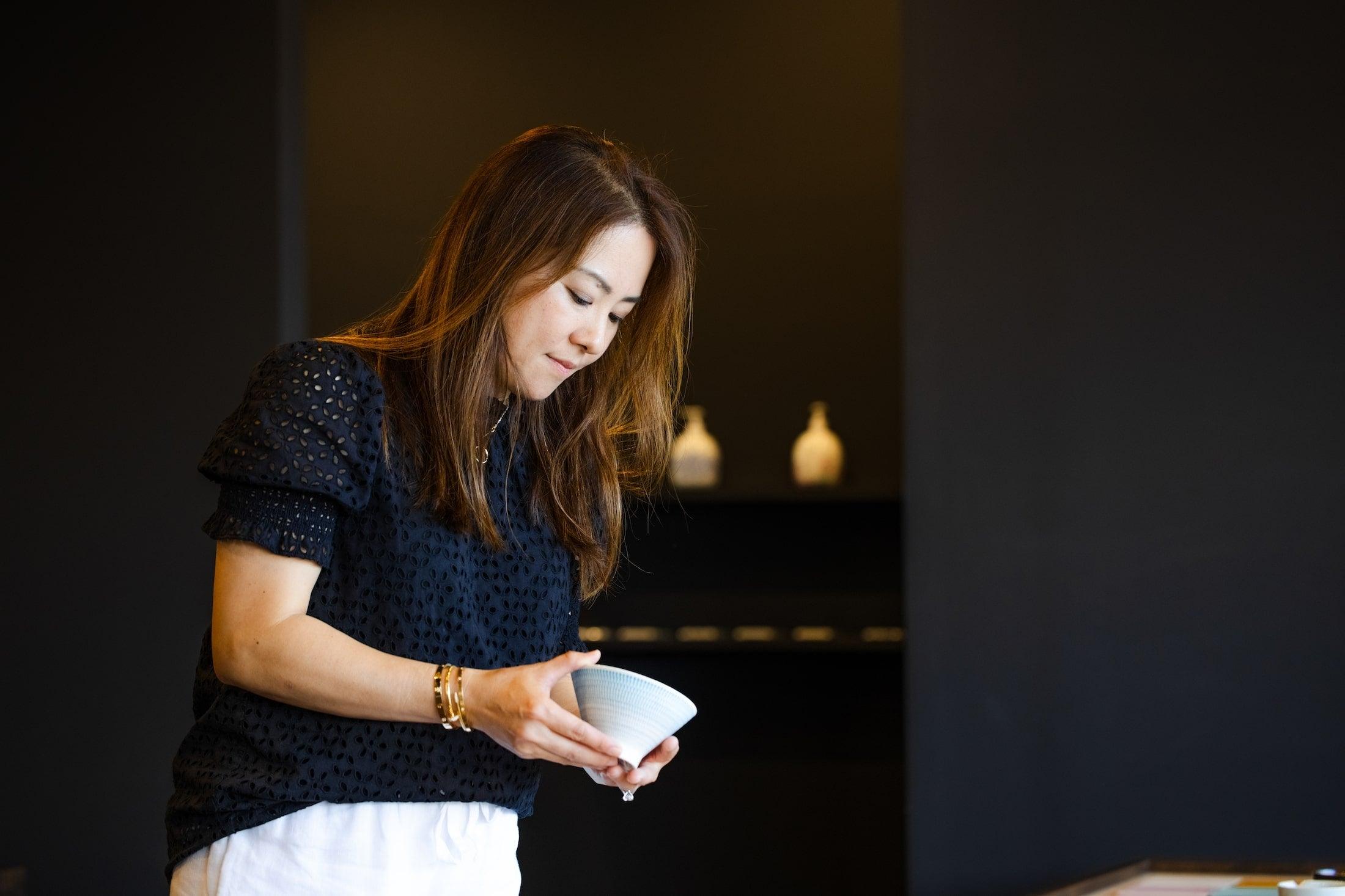 A woman examining a bowl in a shop with a dark background, focused on the item in her hands.
