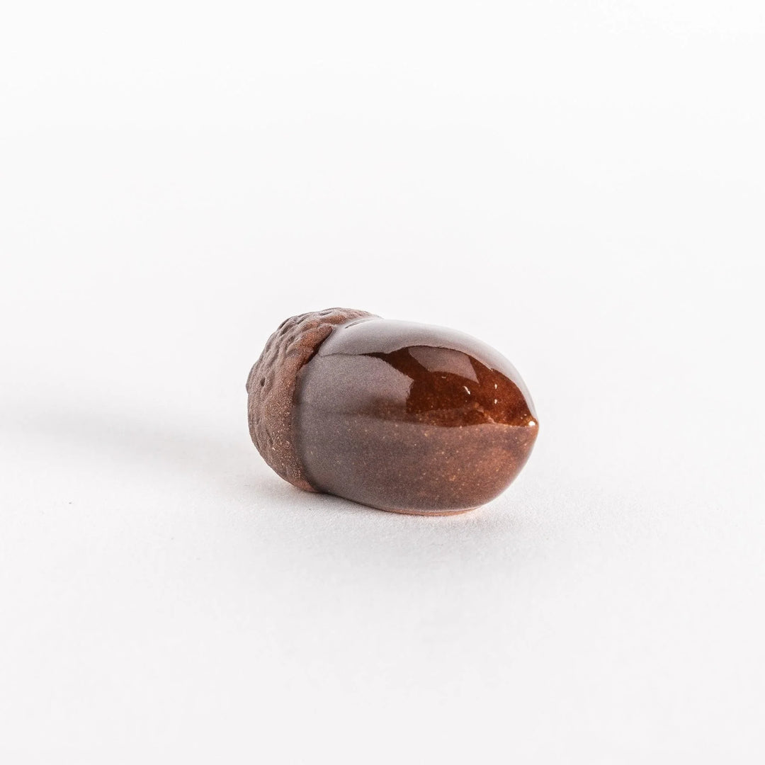 A side view of the ceramic acorn chopstick rest, showing its glossy brown finish and detailed textured top.