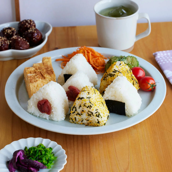 Japanese onigiri rice balls with umeboshi seaweed and furikake served with tamagoyaki vegetables and tea on a wooden table