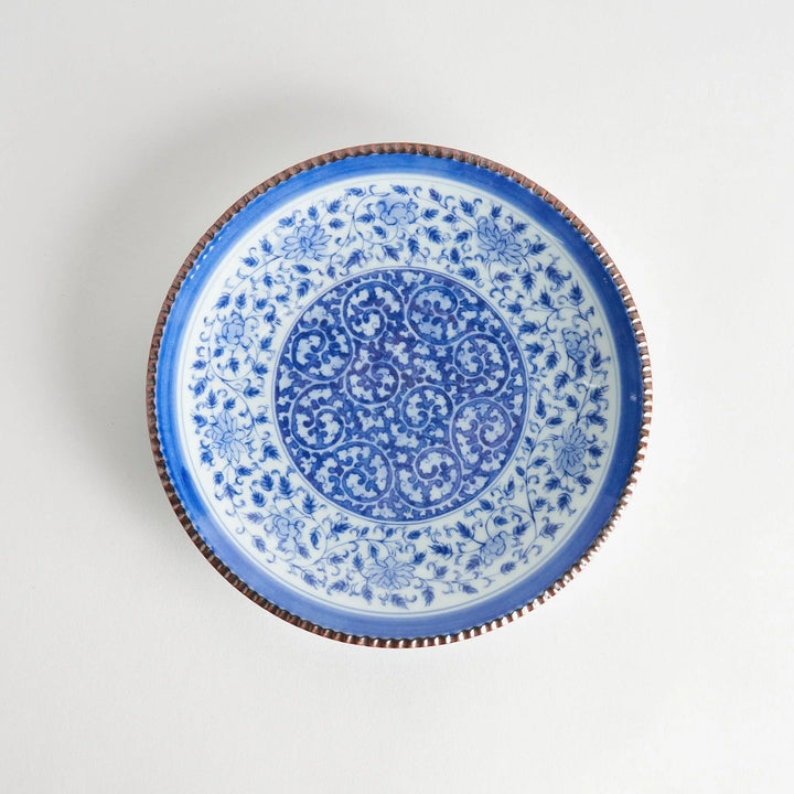Ceramic plate with intricate blue floral design and bold circular motif framed by copper textured rim.