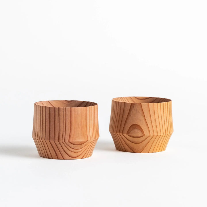 Two Artisan Cedar Sake Cups, showcasing their elegant design with smooth wood grain and a distinctive tapered shape.