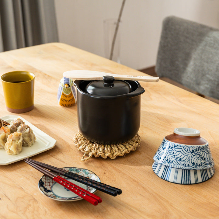 Small artisan straw trivet holding Japanese donabe rice pot on wooden table