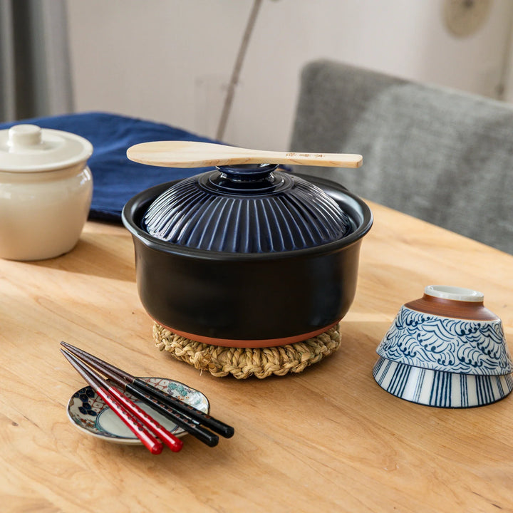 Medium artisan straw trivet supporting Japanese donabe on wooden table