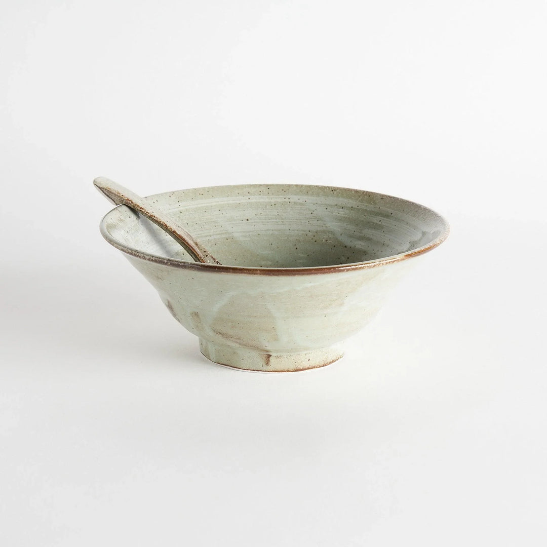 A hand holding a whale and wave patterned ramen bowl and spoon, with additional bowls in the background.