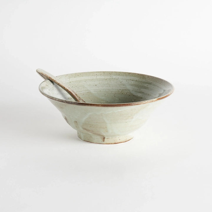 A hand holding a whale and wave patterned ramen bowl and spoon, with additional bowls in the background.
