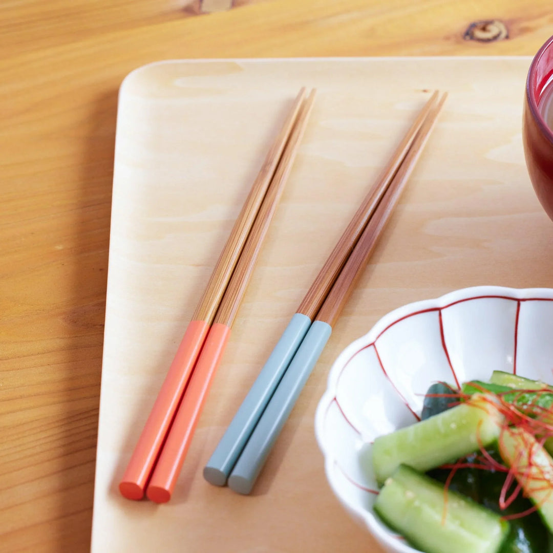 Two pairs of wooden chopsticks—one with coral red handles and the other with muted blue handles.