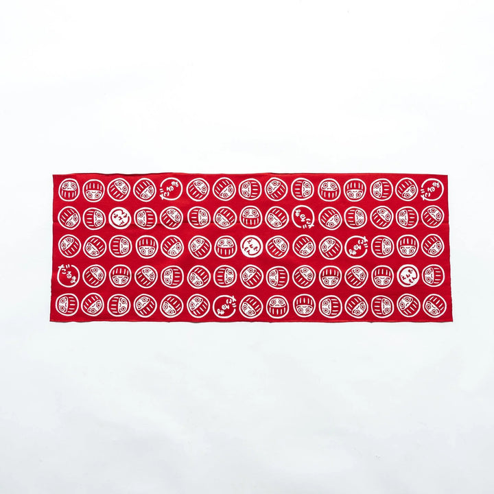 Fully spread-out red tenugui showcasing white Daruma patterns in a repeating design against a white background.