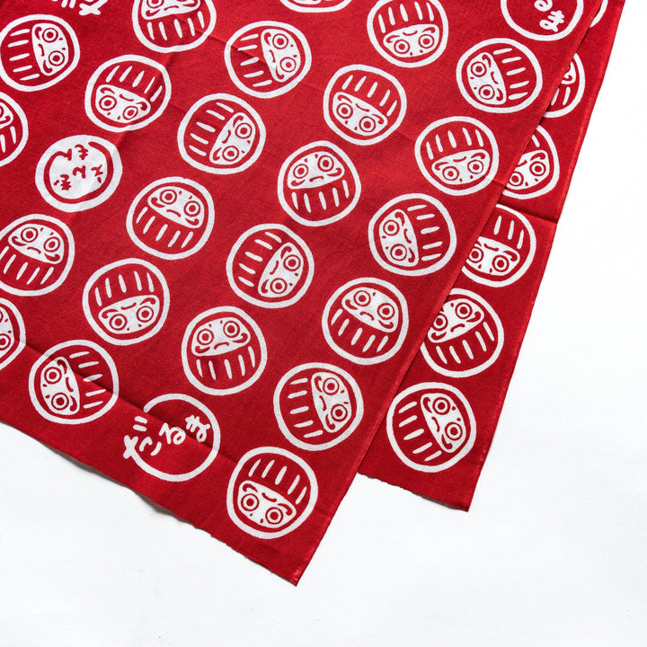 Close-up of the red tenugui showing detailed white Daruma patterns, highlighting the intricate design elements.