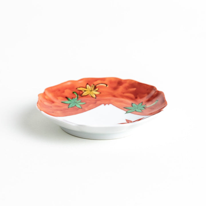 A white dish with a bright red border Mount Fuji, decorated with colorful maple leaves in red, yellow, and green.
