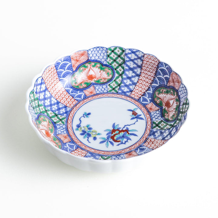 Round deep cereal bowl with scalloped rim floral center and blue red green patterns on white background.