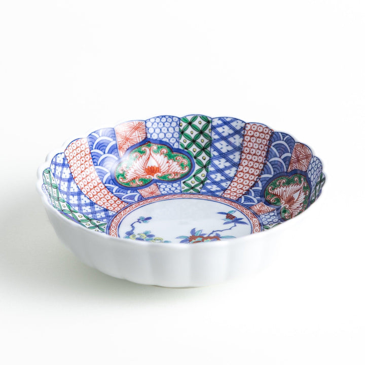 Round deep cereal bowl with scalloped rim floral center and blue red green patterns on white background.