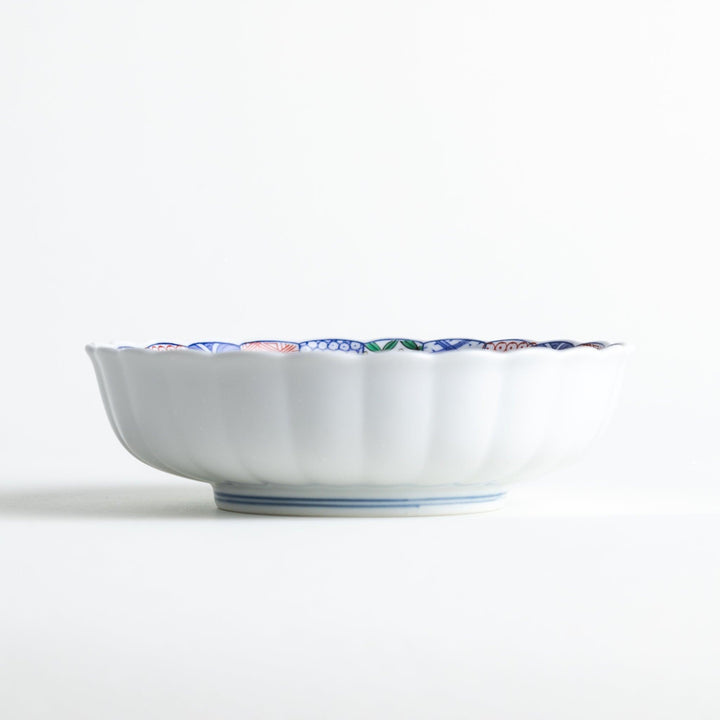 Round deep cereal bowl with scalloped rim floral center and blue red green patterns on white background.