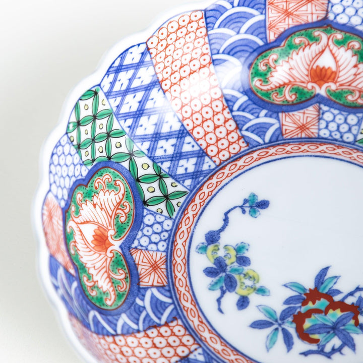 Round deep cereal bowl with scalloped rim floral center and blue red green patterns on white background.