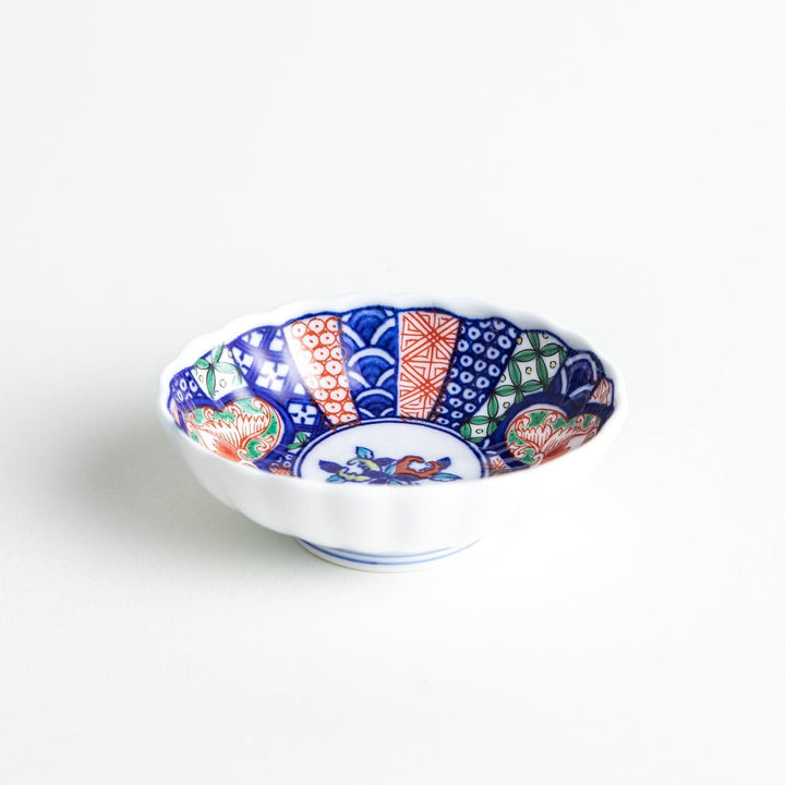 Small scalloped condiment bowl with floral motif and colorful geometric blue red and green patterns.