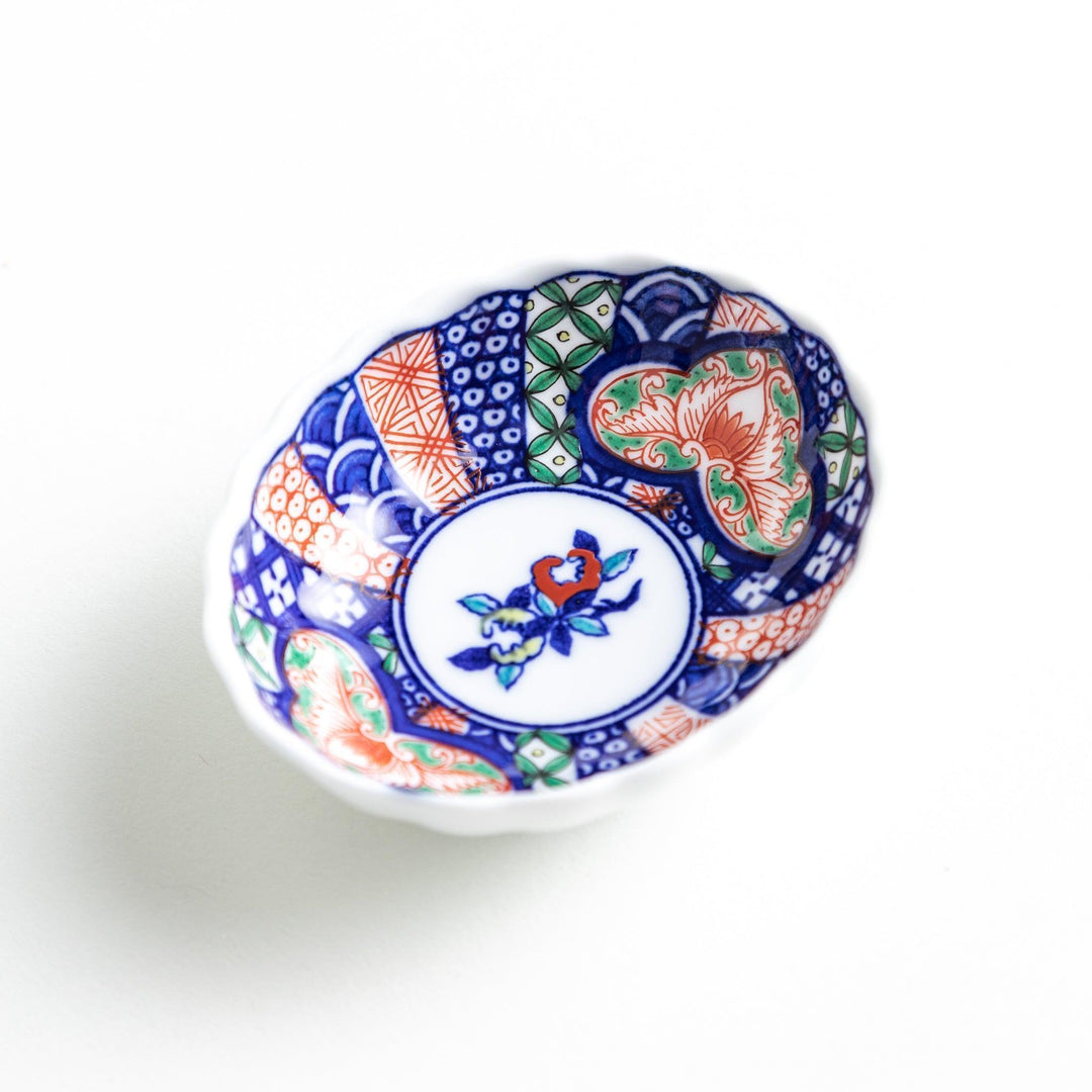 Small scalloped condiment bowl with floral motif and colorful geometric blue red and green patterns.