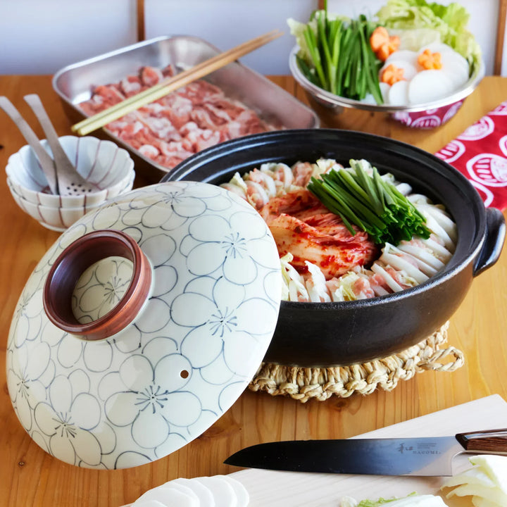 Japanese donabe clay pot with floral lid filled with kimchi nabe of pork napa cabbage and vegetables.