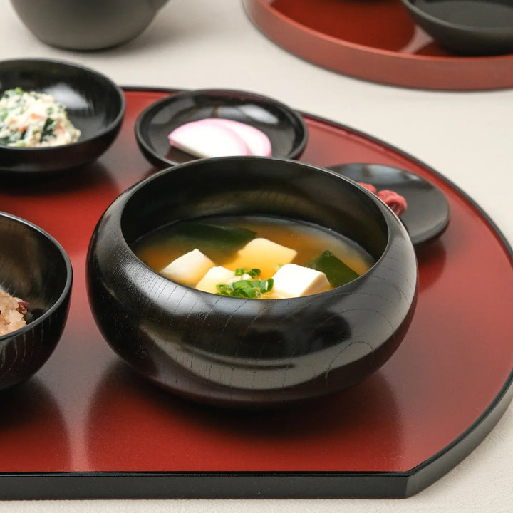 Black lacquered oryoki bowl filled with tofu miso soup showcasing fine wood grain and glossy handcrafted finish