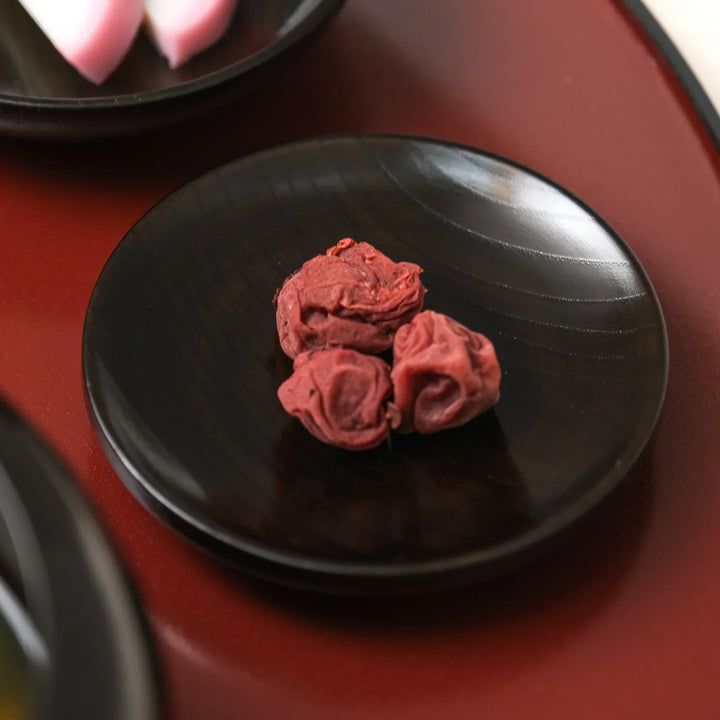 Small black lacquered oryoki dish with red umeboshi pickled plums served as part of a Japanese meal set