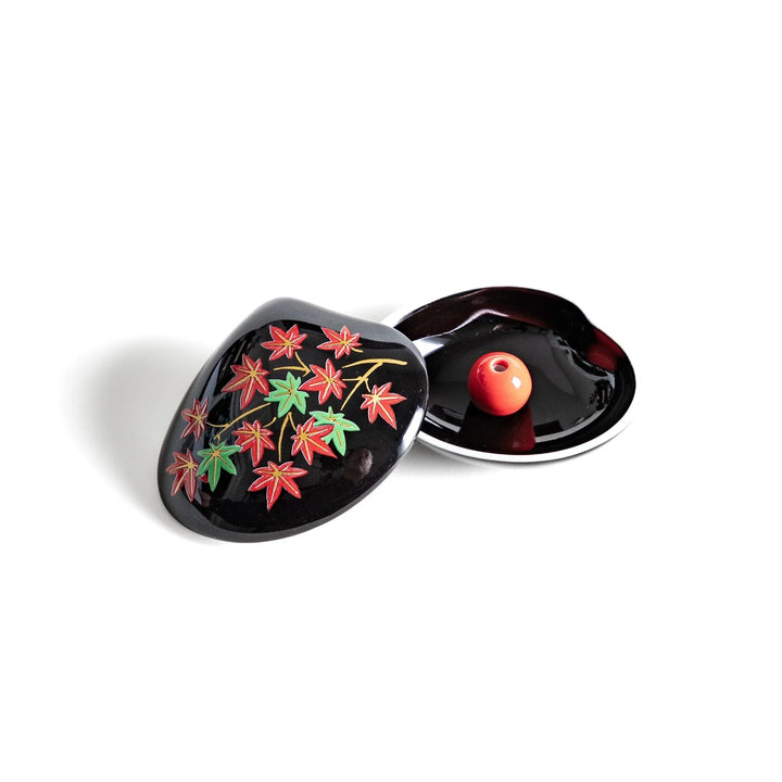 Black seashell-shaped ceramic incense holder with red and green maple leaves and glossy red holder for incense.