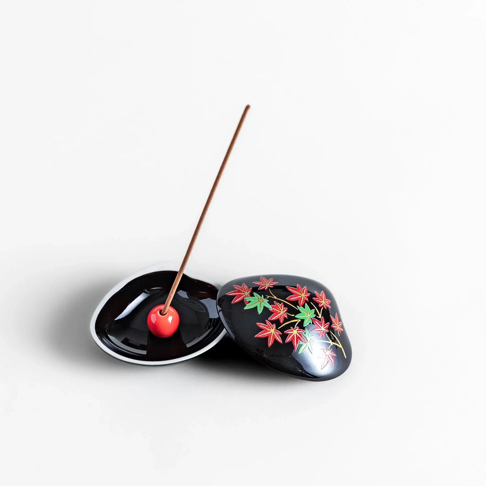 Black seashell-shaped ceramic incense holder with red and green maple leaves and glossy red holder for incense.