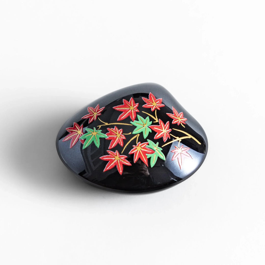 Black seashell-shaped ceramic incense holder with red and green maple leaves and glossy red holder for incense.