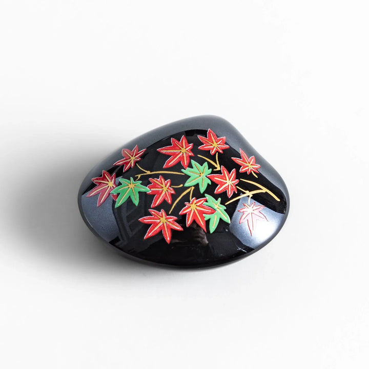 Black seashell-shaped ceramic incense holder with red and green maple leaves and glossy red holder for incense.